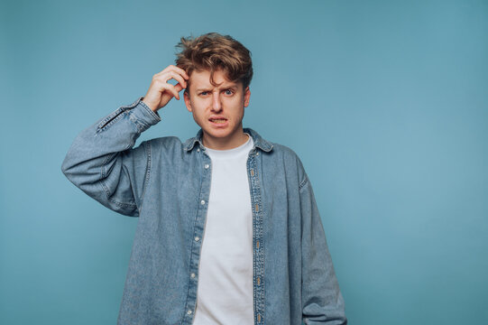 Confused young man scratching his head against a blue background while pondering a perplexing question or situation