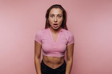Woman expresses surprise in fitness attire against a pink background during a photoshoot