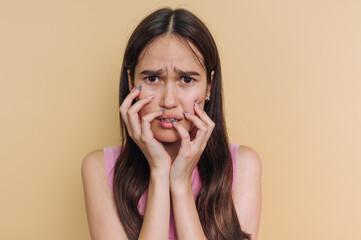 Young woman shows anxiety while touching her face in front of a plain background during a creative...