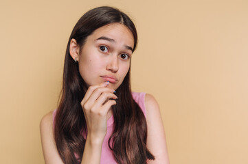 Fototapeta premium Young woman with long hair poses thoughtfully against a yellow background during a casual indoor moment