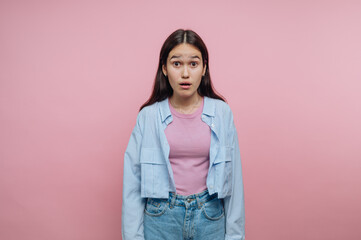 Young woman with long dark hair looks surprised with a pink background during a casual indoor...