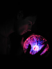 A guy holds a red and blue plasma ball with rays in his hands in the dark close up	
