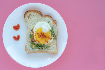 Sandwich with sunny side up egg served on ceramic plate with ketchup in the form of hearts. Top view.
