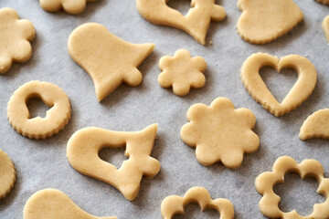 Shapes cut out from raw pastry dough on a sheet of baking paper - preparation of gingerbread...