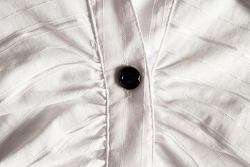 Closeup of pleated white shirt with black button
