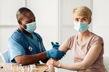 Adult african american lady sitting at doctor's office and getting modern Covid 19 shot injection...