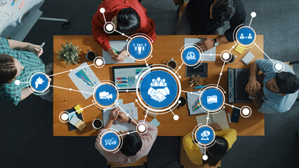 This overhead image captures a collaborative business meeting with diverse professionals, highlighting digital icons representing B2B concepts and teamwork strategies. Amity