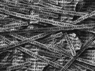 Strips of newspaper with the words Cyberbullying typed on them. Black and white. Close up.