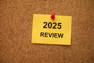 A yellow paper note with the text 2025 Review on it pinned to a cork board. Close up.