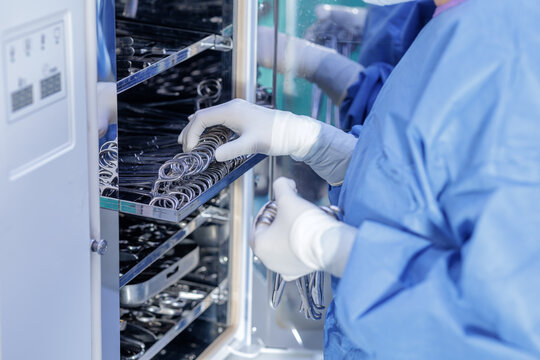 Gloved technician loading surgical instruments into hospital autoclave sterilizer