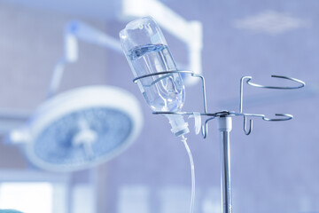 IV drip bottle on stand in operating theatre with surgical light bokeh
