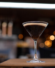 A beautiful dark coffee cocktail served in a margarita glass, set against a blurred bar background, creating a cozy evening atmosphere.