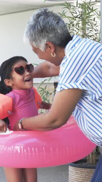 Vertical video: Grandma is reaching for pink swim ring and fitting granddaughter into ring to float