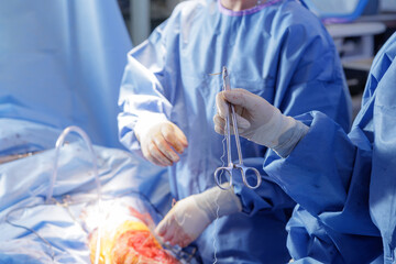 Surgeon holding hemostat with suture during emergency surgery in operating room