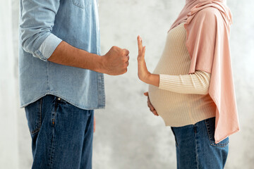 Domestic abuse concept. Muslim husband threatening pregnant wife with fist, woman try to defense,...