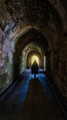Fototapeta premium A shadowy figure walks a long, arched stone hallway