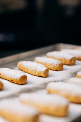 Freshly baked cream rolls sprinkled with powdered sugar on a metal tray in bakery