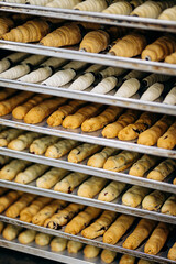 Assortment of croissants, eclairs, and pastry tubes on metal trays in bakery kitchen