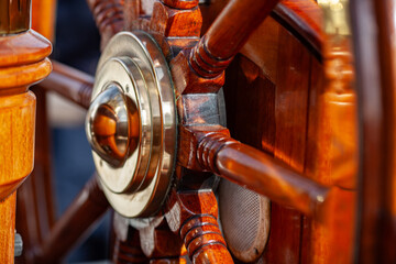 Traditional polished wooden ship wheel with brass hub on sailing vessel – nautical navigation and maritime craftsmanship detail.