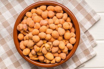 Peanuts in a crispy crust in bowl on checkered napkin.