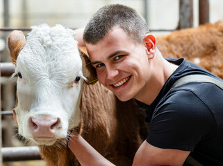 Close up of smiling man working on farm petting baby cow
