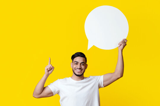Inspired arab guy holding empty communication bubble and pointing finger up, yellow studio background. Happy middle-eastern young man in casual with blank clipart, sharing creative ideas, panorama