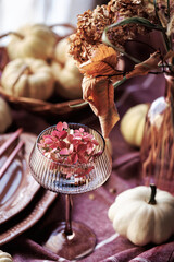 A cozy Thanksgiving tablescape with white pumpkins, a glass goblet with pink flowers, and a rustic napkin arrangement, perfect for fall gatherings and seasonal invitations