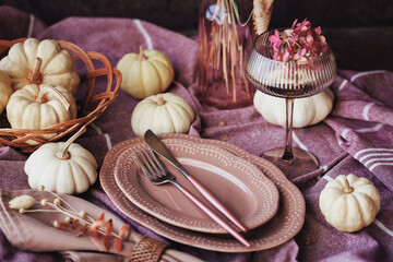 A beautifully arranged autumn table setting with white pumpkins, a ribbed glass filled with pink flowers, and rustic tableware, ideal for Thanksgiving and seasonal dining inspiration