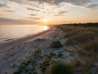 Aerial drone view of a bikepacking camp with a tent on a sandy Baltic Sea beach in Estonia at sunset.