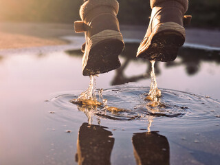 Brown boots jumping in a puddle on a wet street. Close-up action shot capturing water droplets and...