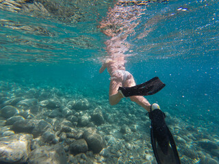 Underwater view of a woman with fins snorkeling in the clear turquoise sea on a sunny summer...