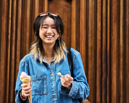 Portrait of a smiling young woman girl eating an ice cream walking in the city, tourists visiting destination, summer trip exploring, posing in front of a wooden gate door wall