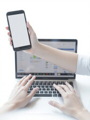 a person holding a smartphone in one hand and typing on a laptop with the other. The laptop screen displays a webpage