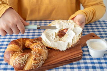 Beigel covered with creamy cheese on the hands of a child for tasty snack.