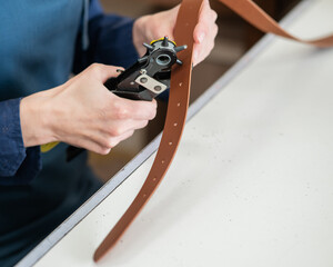 A woman makes holes in a leather belt. Leatherworker's workshop. 