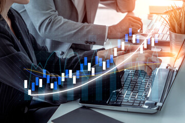 A close-up view of business professionals analyzing financial data on laptops, with digital stock market graphics overlaying their collaboration in a sleek office space. Impute