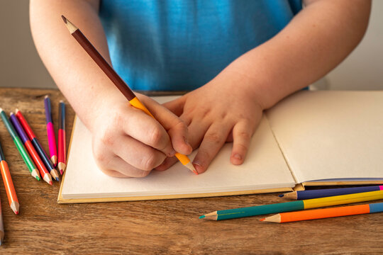 Child draws with pencil in a sketchbook. Hands of a child and pencil on the background of blank paper.