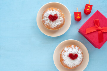 Jewish holiday Hanukkah concept with red gift box, traditional dreidels, tasty doughnuts Sufganiyah on blue wooden background. Hebrew letters on dreidels say: 
