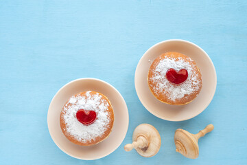 Traditional Hanukkah donuts Sufganiyah, wooden dreidels on blue background. Pastries for Jewish holiday Hanukkah.