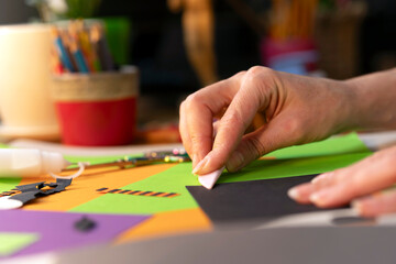 Fototapeta premium Close-up of a woman’s hand folding and pressing black paper on colorful sheets while crafting decorations.