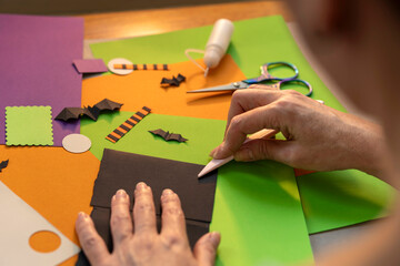 Over the shoulder view of a woman folding black paper with a crafting tool on colorful sheets and...