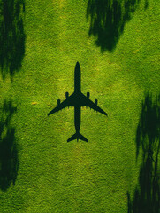 Aerial silhouette of an oversized airplane casting a shadow on vibrant green grass with scattered trees