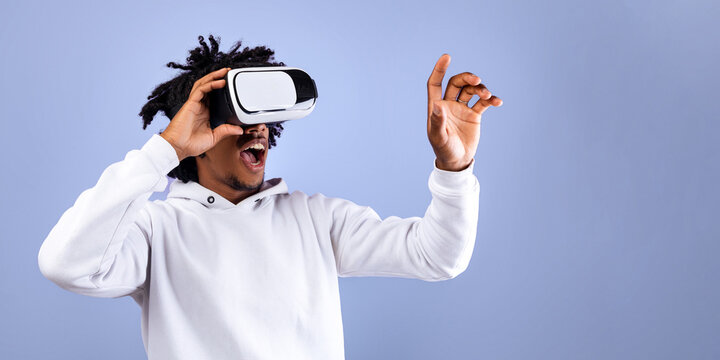 Amazed African American teen guy in VR headset using virtual reality, touching imaginary screen on violet background. Funky black adolescent exploring cyberspace, experiencing modern technologies - Powered by Adobe