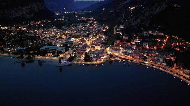 tunning 4K night aerial drone footage of Torbole sul Garda on the northern shore of Lake Garda, Italy. Beautiful illuminated streets, vibrant city lights, hotels, restaurants, and a relaxing summer 