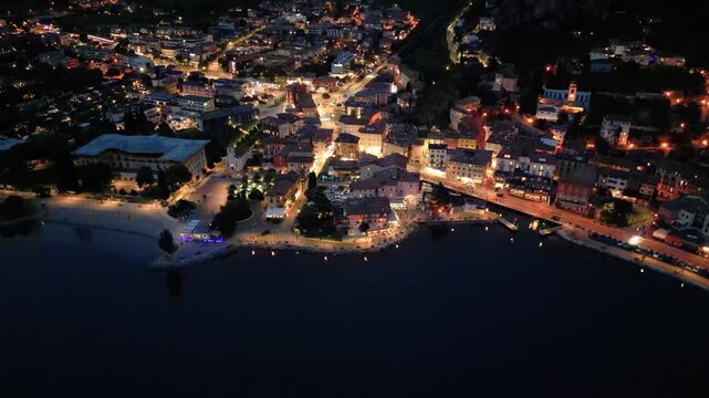 tunning 4K night aerial drone footage of Torbole sul Garda on the northern shore of Lake Garda, Italy. Beautiful illuminated streets, vibrant city lights, hotels, restaurants, and a relaxing summer 
