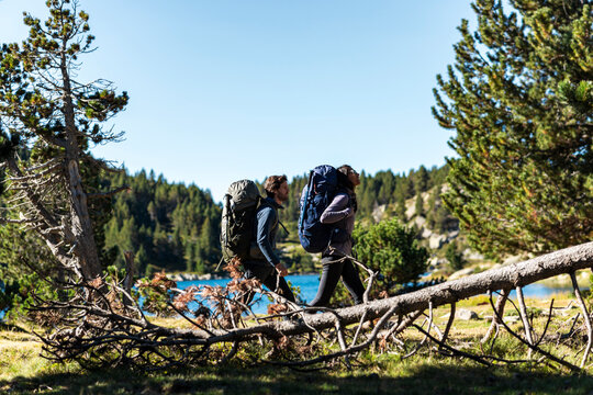 Couple of hikers walking side by side with backpacks near mountain lake