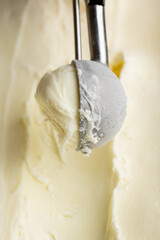 Vanilla ice cream scoop in metal spoon over creamy background, macro food texture shot