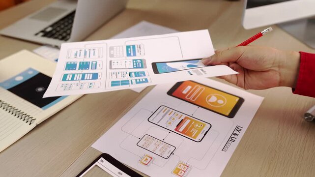 Excellent startup company employee presenting user interface prototype for mobile application to smart co-worker in office workspace. UX UI designer explain function of icon design on paper. Synergic