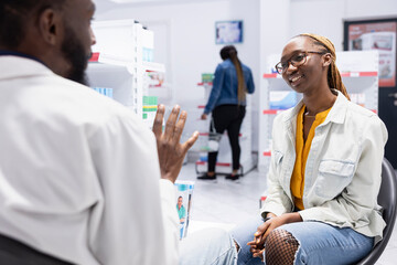Obraz premium Pharmacy worker assisting a customer with detailed pharmacist advice, explaining medicine and health products in a busy retail drugstore. Pharmaceutical care and patient wellbeing.