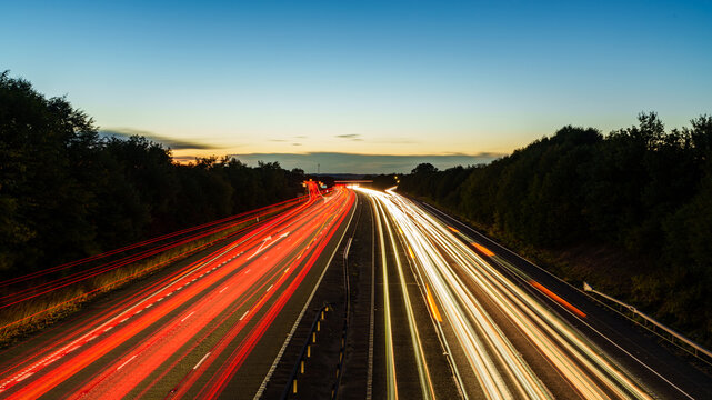 Light trails illuminating highway at dusk with colorful sunset - Powered by Adobe